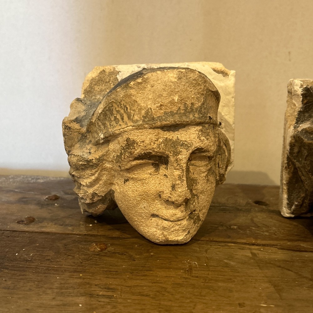 A pair of 15th-century carved limestone corbels depicting human heads with weathered facial features and period headwear. View III