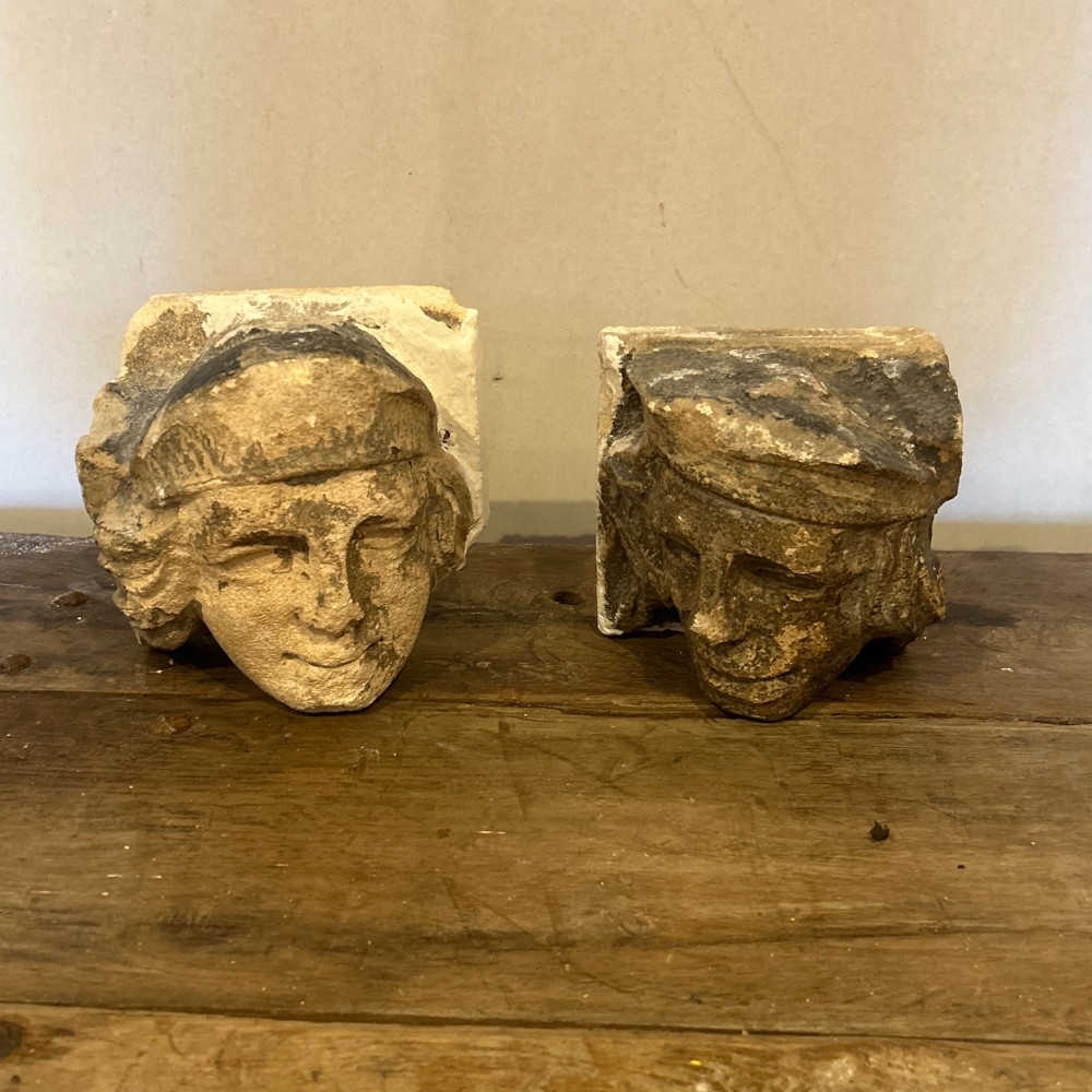 A pair of 15th-century carved limestone corbels depicting human heads with weathered facial features and period headwear. View IV