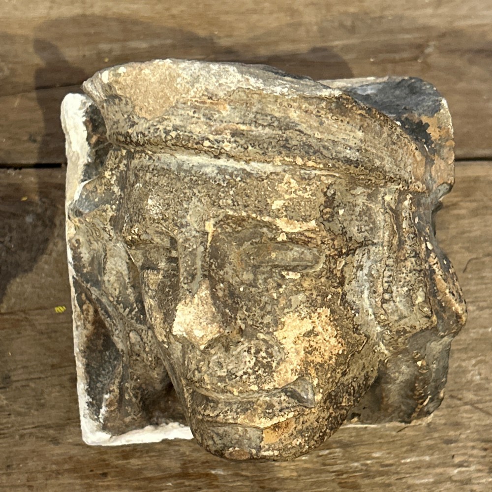 A pair of 15th-century carved limestone corbels depicting human heads with weathered facial features and period headwear. View V