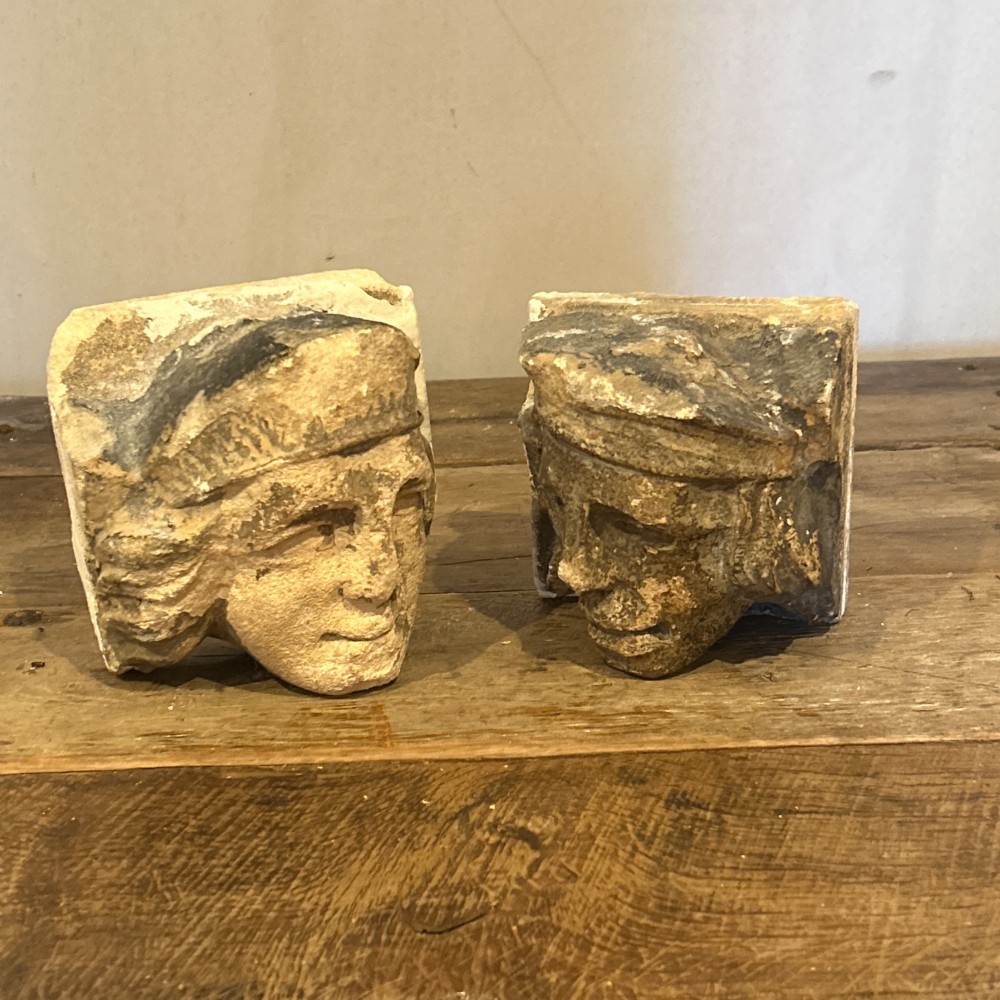 A pair of 15th-century carved limestone corbels depicting human heads with weathered facial features and period headwear. View XIII