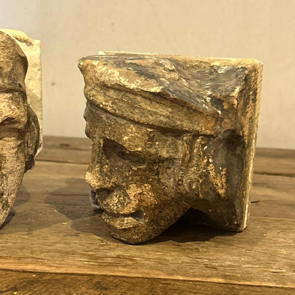 A pair of 15th-century carved limestone corbels depicting human heads with weathered facial features and period headwear. View XIV
