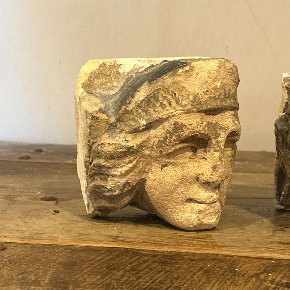 A pair of 15th-century carved limestone corbels depicting human heads with weathered facial features and period headwear. View XV