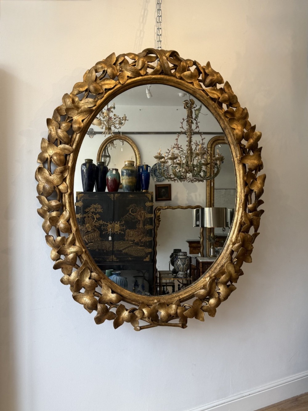 A large 19th-century oval wall mirror featuring a carved giltwood frame decorated with sculptural overlapping leaf motifs.