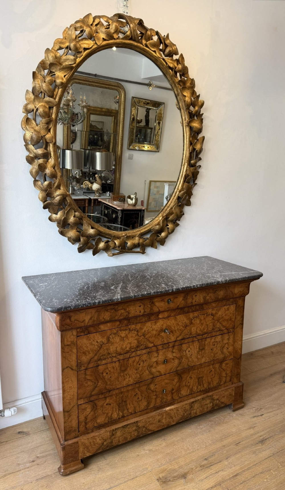 A large 19th-century oval wall mirror featuring a carved giltwood frame decorated with sculptural overlapping leaf motifs. View II