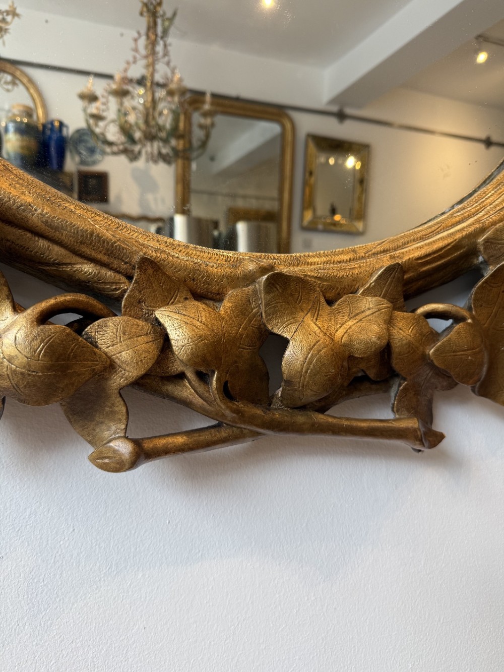 A large 19th-century oval wall mirror featuring a carved giltwood frame decorated with sculptural overlapping leaf motifs. View VI