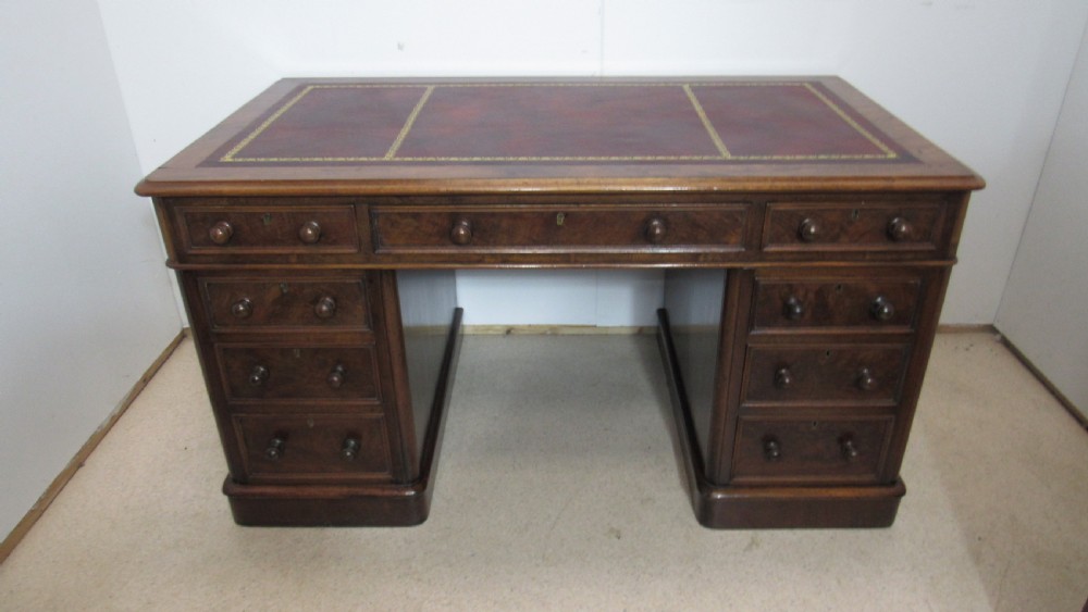 An antique mahogany pedestal desk featuring a red leather writing surface with gold tooling and nine drawers fitted with turned wooden handles.