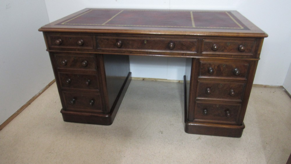 An antique mahogany pedestal desk featuring a red leather writing surface with gold tooling and nine drawers fitted with turned wooden handles. View II