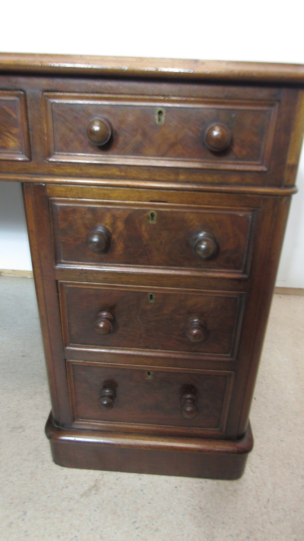 An antique mahogany pedestal desk featuring a red leather writing surface with gold tooling and nine drawers fitted with turned wooden handles. View III