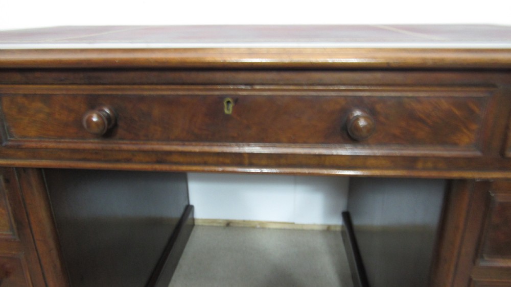 An antique mahogany pedestal desk featuring a red leather writing surface with gold tooling and nine drawers fitted with turned wooden handles. View IV