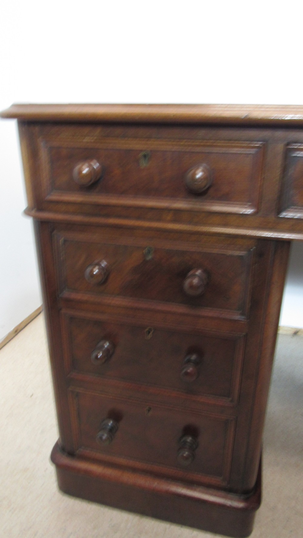 An antique mahogany pedestal desk featuring a red leather writing surface with gold tooling and nine drawers fitted with turned wooden handles. View V