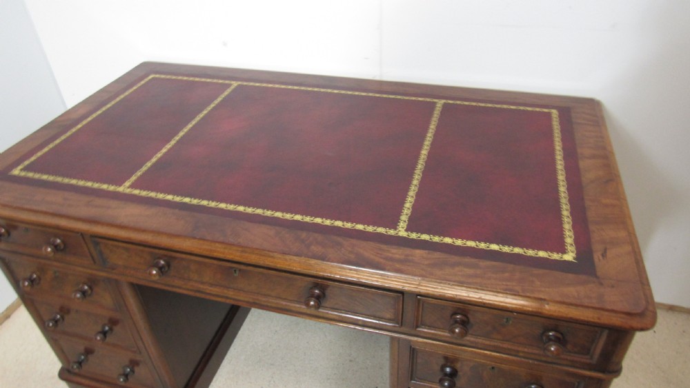 An antique mahogany pedestal desk featuring a red leather writing surface with gold tooling and nine drawers fitted with turned wooden handles. View VI