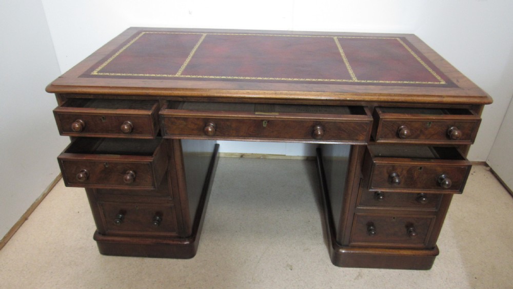 An antique mahogany pedestal desk featuring a red leather writing surface with gold tooling and nine drawers fitted with turned wooden handles. View VII