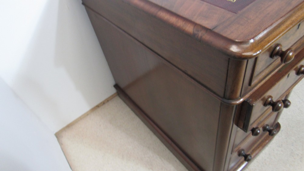 An antique mahogany pedestal desk featuring a red leather writing surface with gold tooling and nine drawers fitted with turned wooden handles. View IX