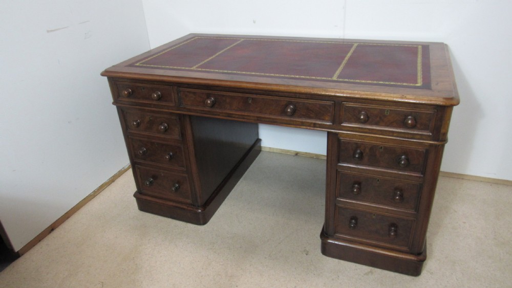 An antique mahogany pedestal desk featuring a red leather writing surface with gold tooling and nine drawers fitted with turned wooden handles. View XVIII