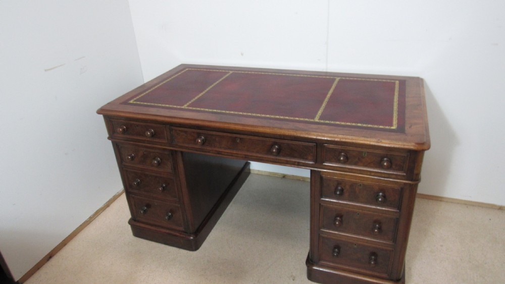An antique mahogany pedestal desk featuring a red leather writing surface with gold tooling and nine drawers fitted with turned wooden handles. View XIX