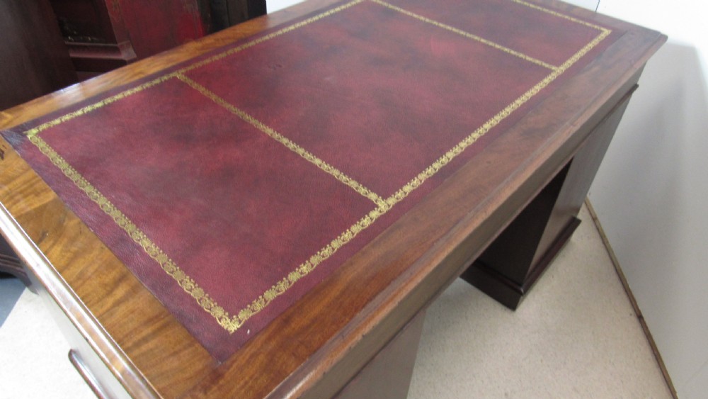 An antique mahogany pedestal desk featuring a red leather writing surface with gold tooling and nine drawers fitted with turned wooden handles. View XXIII