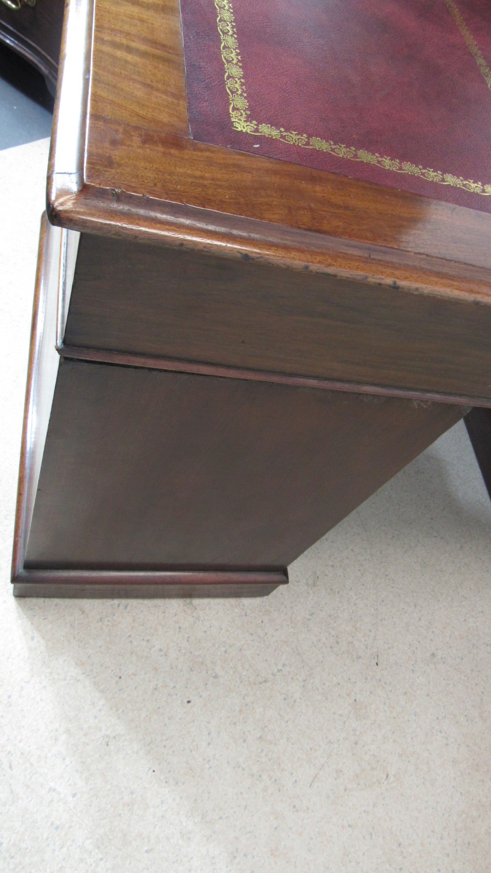 An antique mahogany pedestal desk featuring a red leather writing surface with gold tooling and nine drawers fitted with turned wooden handles. View XXIV