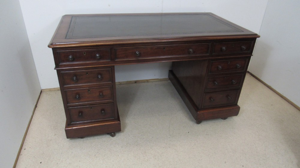 A dark mahogany pedestal desk featuring an inset leather writing surface, multiple drawers fitted with turned wooden knobs, and a central kneehole.