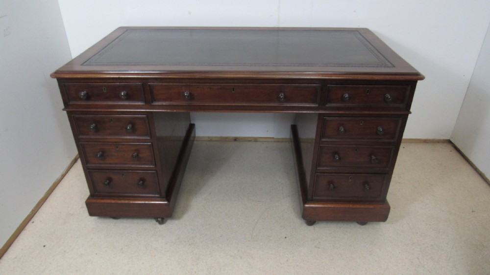 A dark mahogany pedestal desk featuring an inset leather writing surface, multiple drawers fitted with turned wooden knobs, and a central kneehole. View II