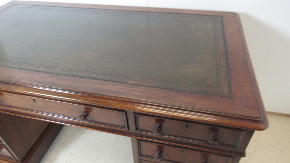 A dark mahogany pedestal desk featuring an inset leather writing surface, multiple drawers fitted with turned wooden knobs, and a central kneehole. View III