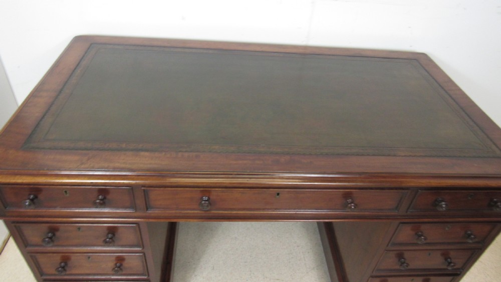A dark mahogany pedestal desk featuring an inset leather writing surface, multiple drawers fitted with turned wooden knobs, and a central kneehole. View IV