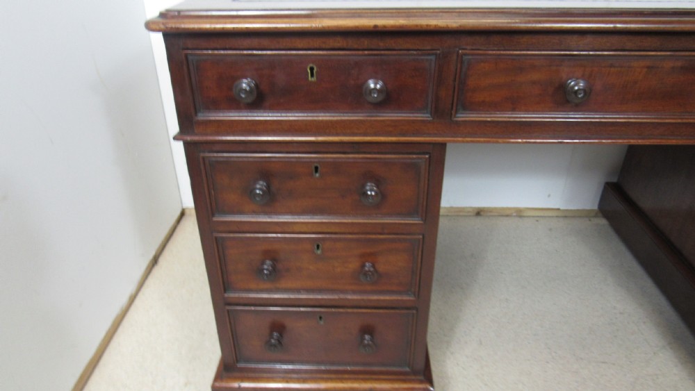 A dark mahogany pedestal desk featuring an inset leather writing surface, multiple drawers fitted with turned wooden knobs, and a central kneehole. View V