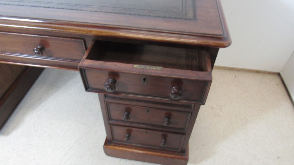 A dark mahogany pedestal desk featuring an inset leather writing surface, multiple drawers fitted with turned wooden knobs, and a central kneehole. View VII