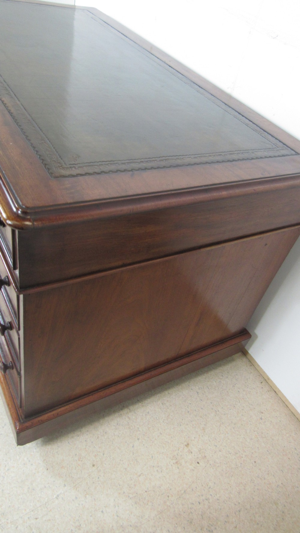 A dark mahogany pedestal desk featuring an inset leather writing surface, multiple drawers fitted with turned wooden knobs, and a central kneehole. View X