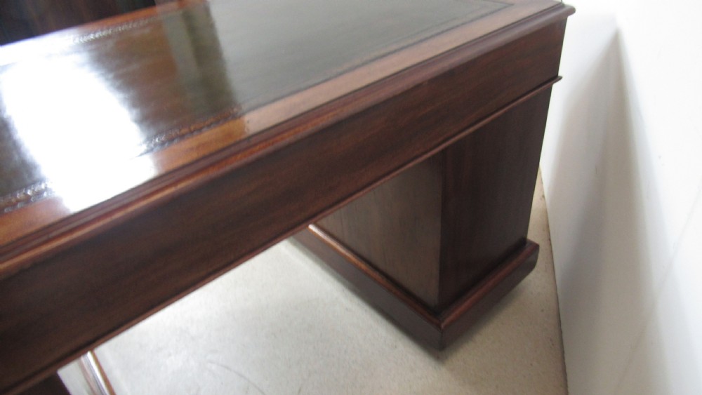 A dark mahogany pedestal desk featuring an inset leather writing surface, multiple drawers fitted with turned wooden knobs, and a central kneehole. View XI