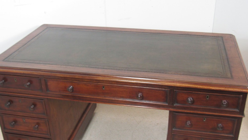 A dark mahogany pedestal desk featuring an inset leather writing surface, multiple drawers fitted with turned wooden knobs, and a central kneehole. View XV