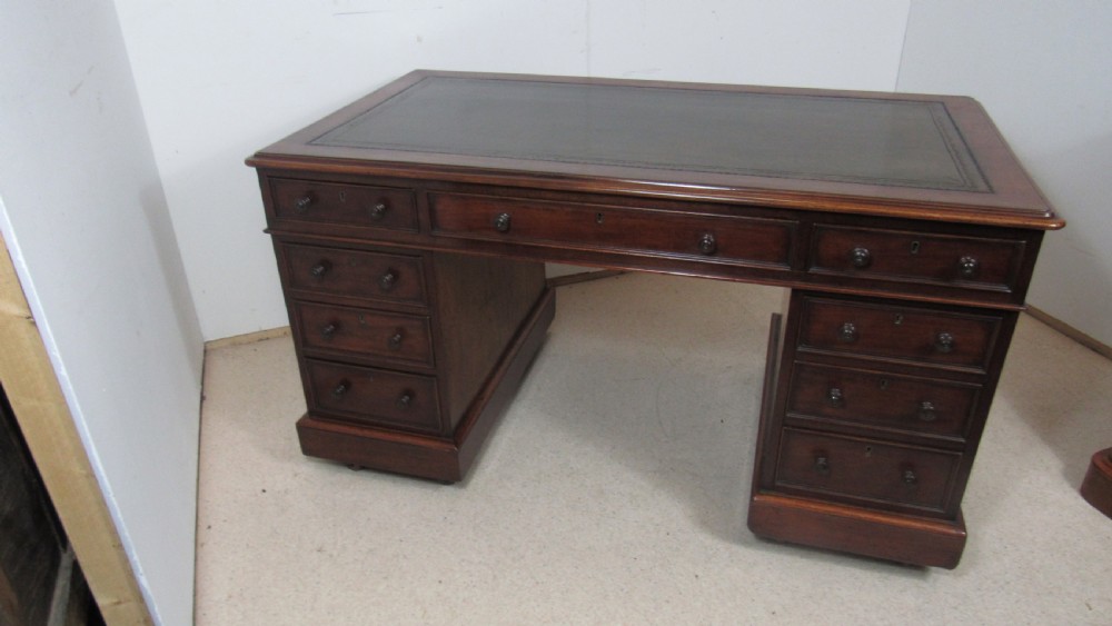 A dark mahogany pedestal desk featuring an inset leather writing surface, multiple drawers fitted with turned wooden knobs, and a central kneehole. View XIX