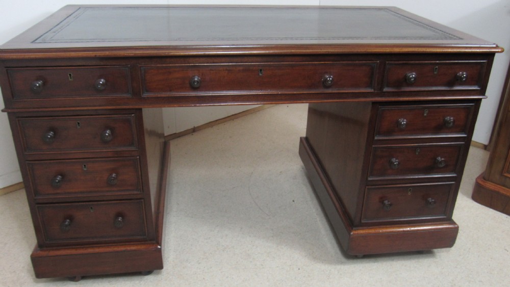 A dark mahogany pedestal desk featuring an inset leather writing surface, multiple drawers fitted with turned wooden knobs, and a central kneehole. View XXI
