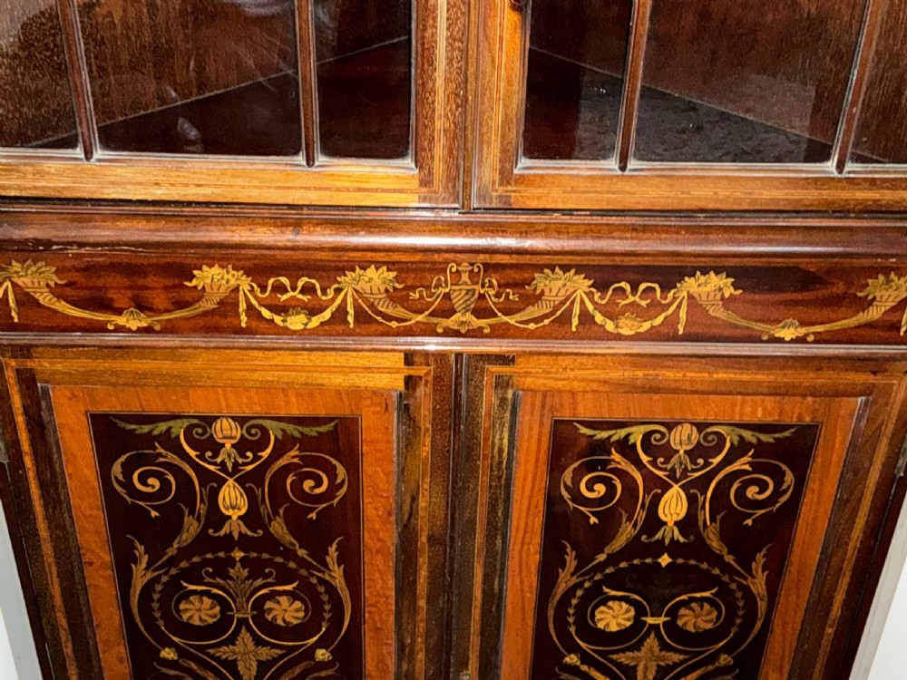 An Edwardian mahogany corner cabinet featuring a broken pediment cresting, astragal glazed upper doors, and detailed floral marquetry inlays on the lower doors. View IX