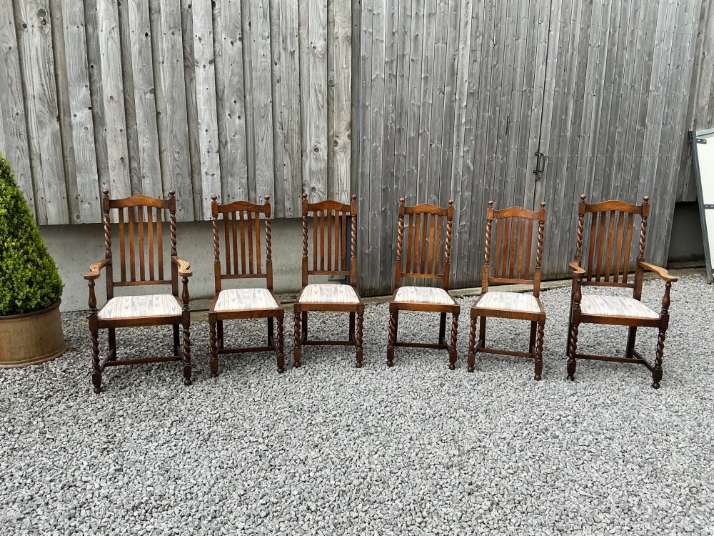 A set of six warm brown oak dining chairs, comprising two carver armchairs and four side chairs, featuring barley twist leg supports and vertical slatted backrests.