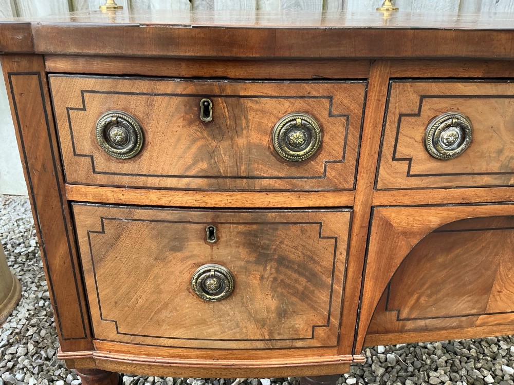 A Regency mahogany bow-front sideboard featuring reeded legs, inlaid drawer fronts with brass ring handles, and a slim brass curtain rail on the top surface. View III