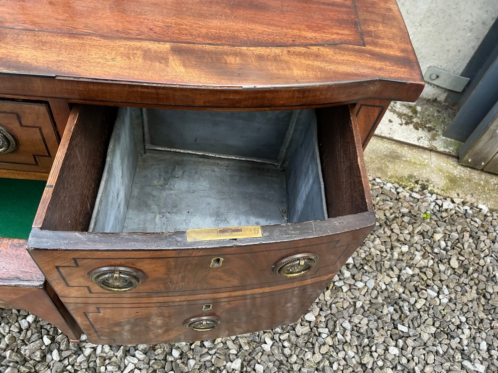 A Regency mahogany bow-front sideboard featuring reeded legs, inlaid drawer fronts with brass ring handles, and a slim brass curtain rail on the top surface. View VII