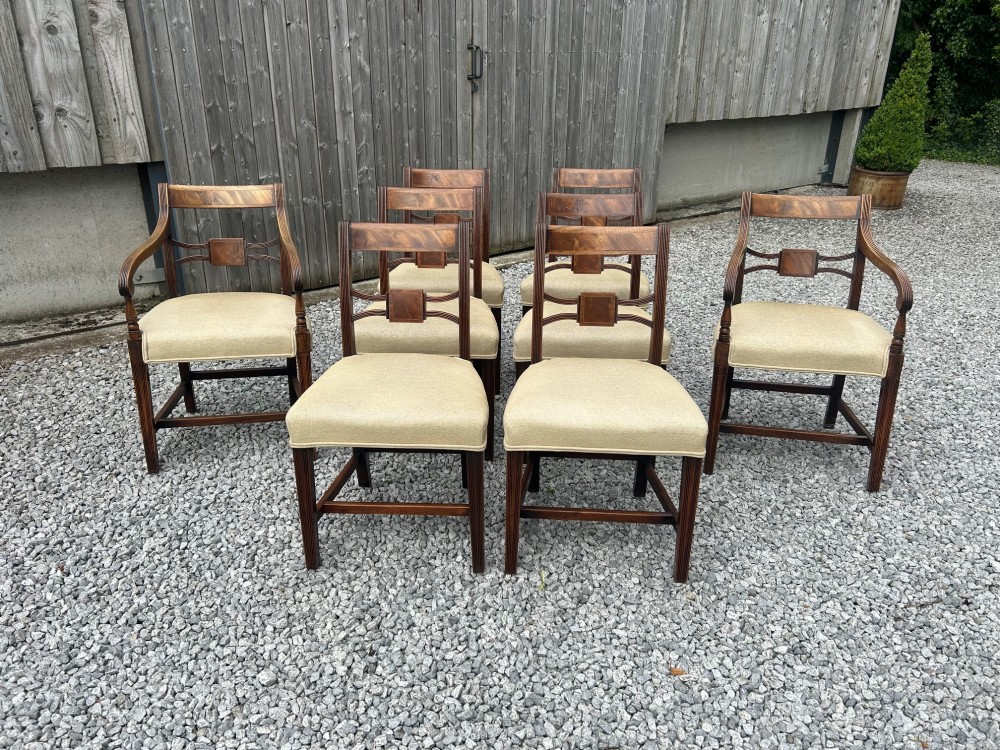 A set of eight Georgian mahogany dining chairs featuring reeded legs, carved bar backs, and beige upholstered seats, comprising six side chairs and two armchairs.
