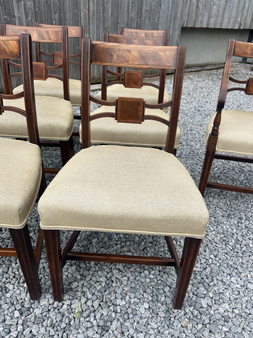 A set of eight Georgian mahogany dining chairs featuring reeded legs, carved bar backs, and beige upholstered seats, comprising six side chairs and two armchairs. View IV