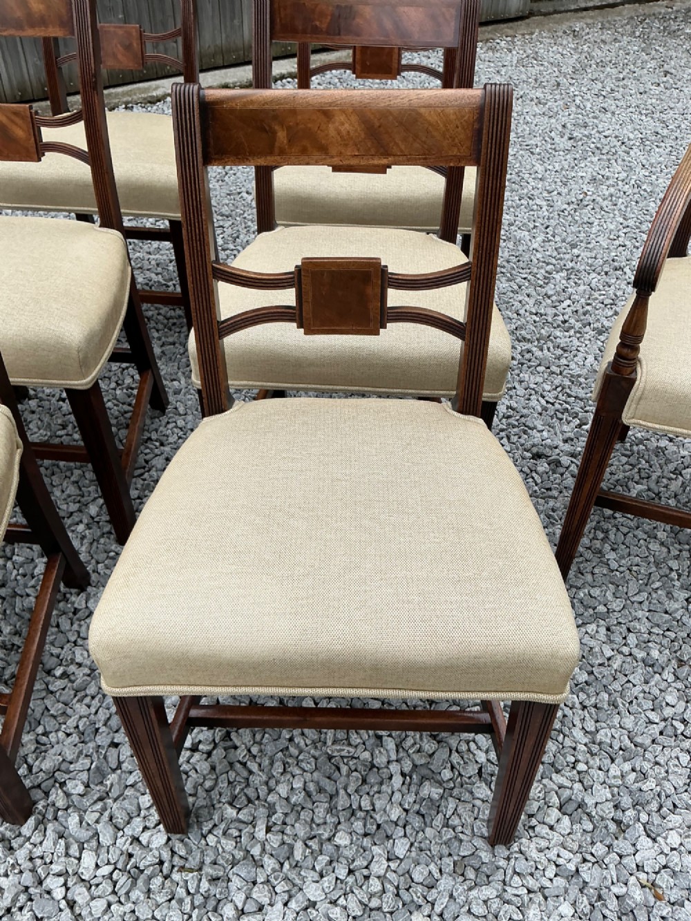 A set of eight Georgian mahogany dining chairs featuring reeded legs, carved bar backs, and beige upholstered seats, comprising six side chairs and two armchairs. View X