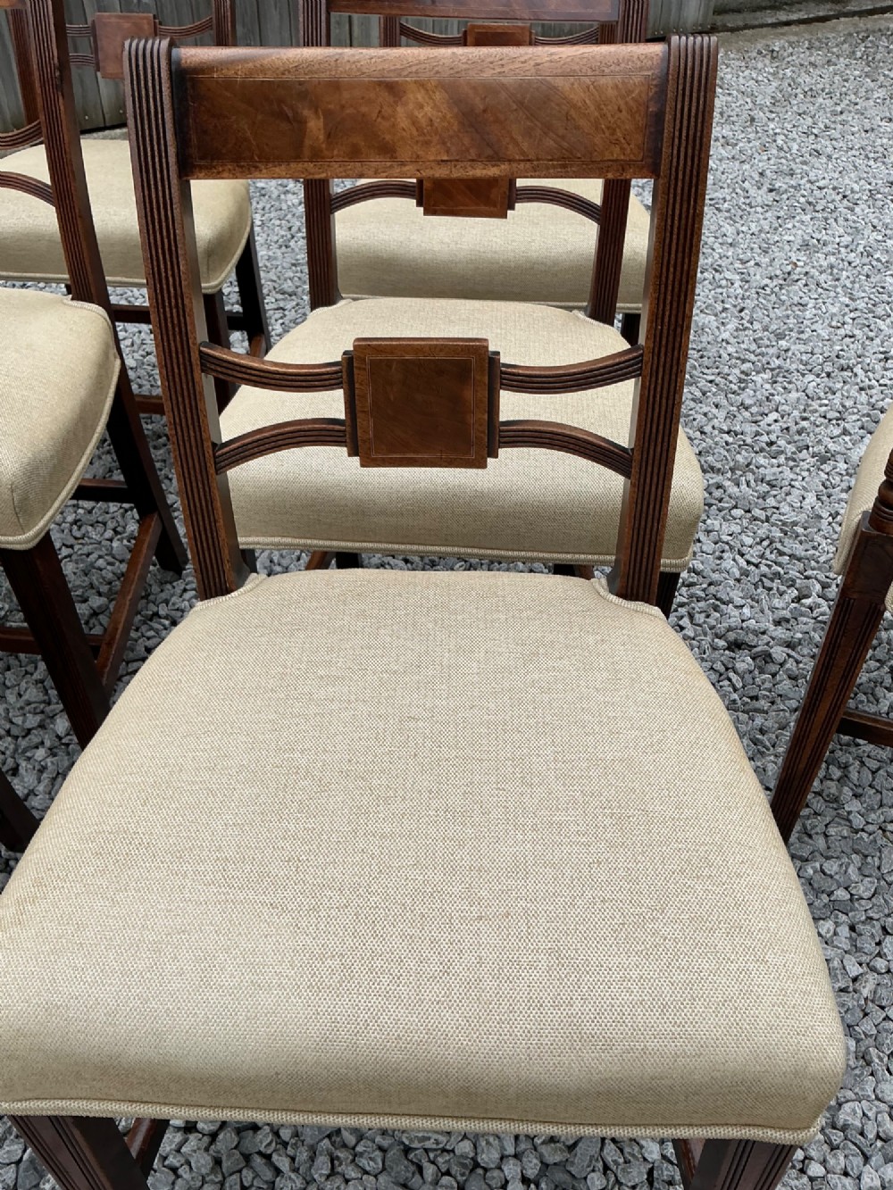 A set of eight Georgian mahogany dining chairs featuring reeded legs, carved bar backs, and beige upholstered seats, comprising six side chairs and two armchairs. View XI