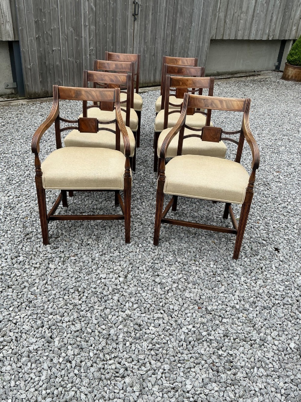 A set of eight Georgian mahogany dining chairs featuring reeded legs, carved bar backs, and beige upholstered seats, comprising six side chairs and two armchairs. View XII