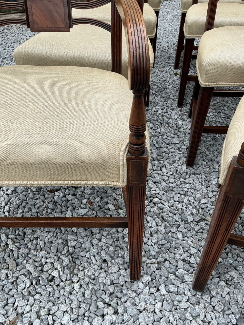 A set of eight Georgian mahogany dining chairs featuring reeded legs, carved bar backs, and beige upholstered seats, comprising six side chairs and two armchairs. View XV