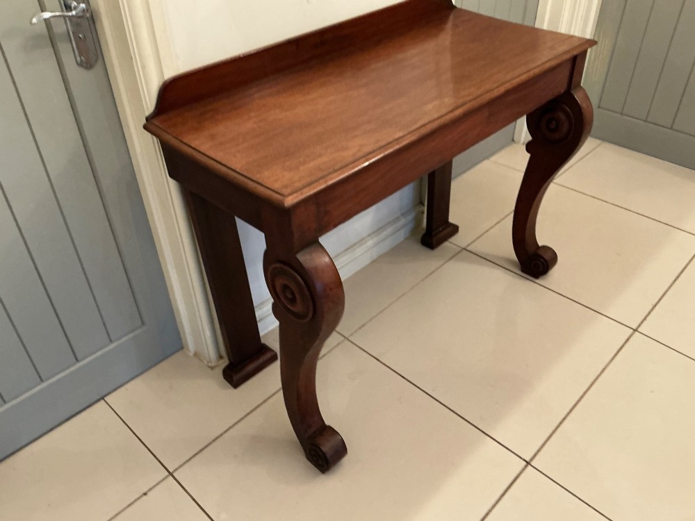 A William IV mahogany console table featuring curved scroll front legs, a low rear gallery, and a polished rectangular top. View II