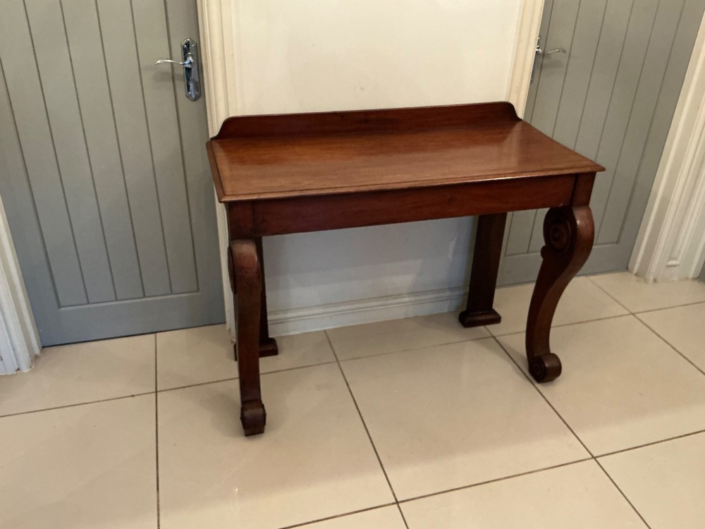 A William IV mahogany console table featuring curved scroll front legs, a low rear gallery, and a polished rectangular top. View VII