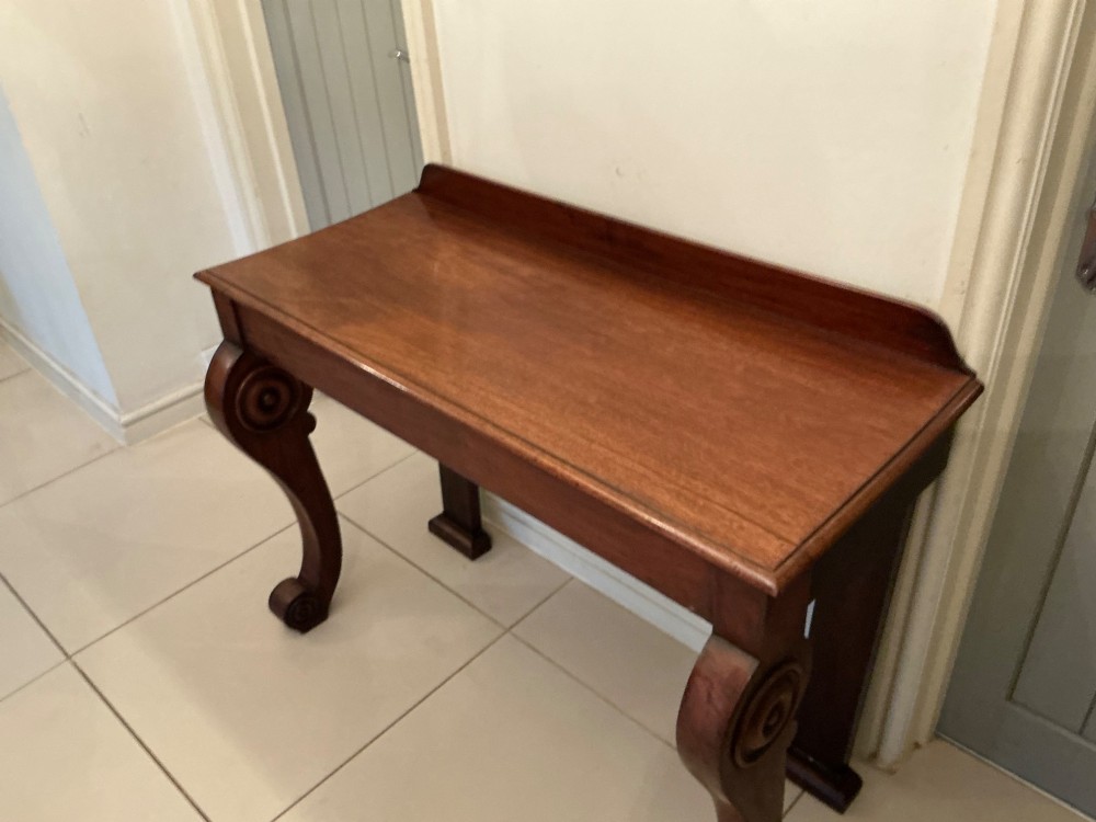 A William IV mahogany console table featuring curved scroll front legs, a low rear gallery, and a polished rectangular top. View VIII