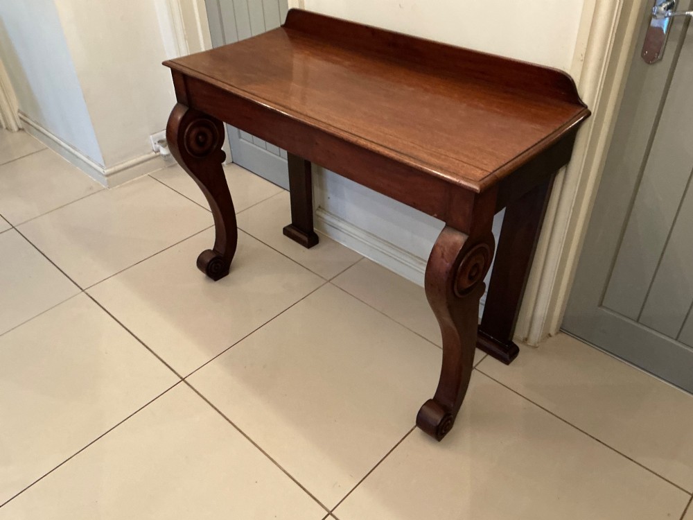 A William IV mahogany console table featuring curved scroll front legs, a low rear gallery, and a polished rectangular top. View X