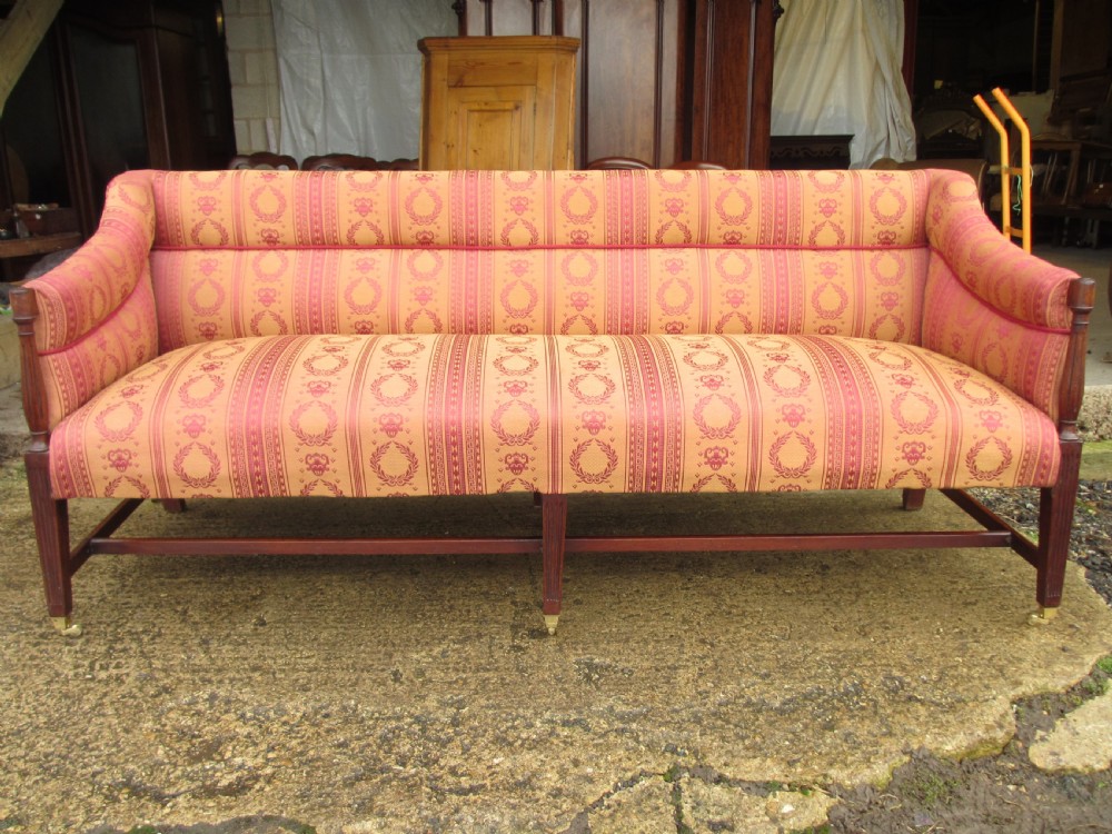 A Regency mahogany framed sofa upholstered in patterned red and gold fabric with reeded legs and brass castors.