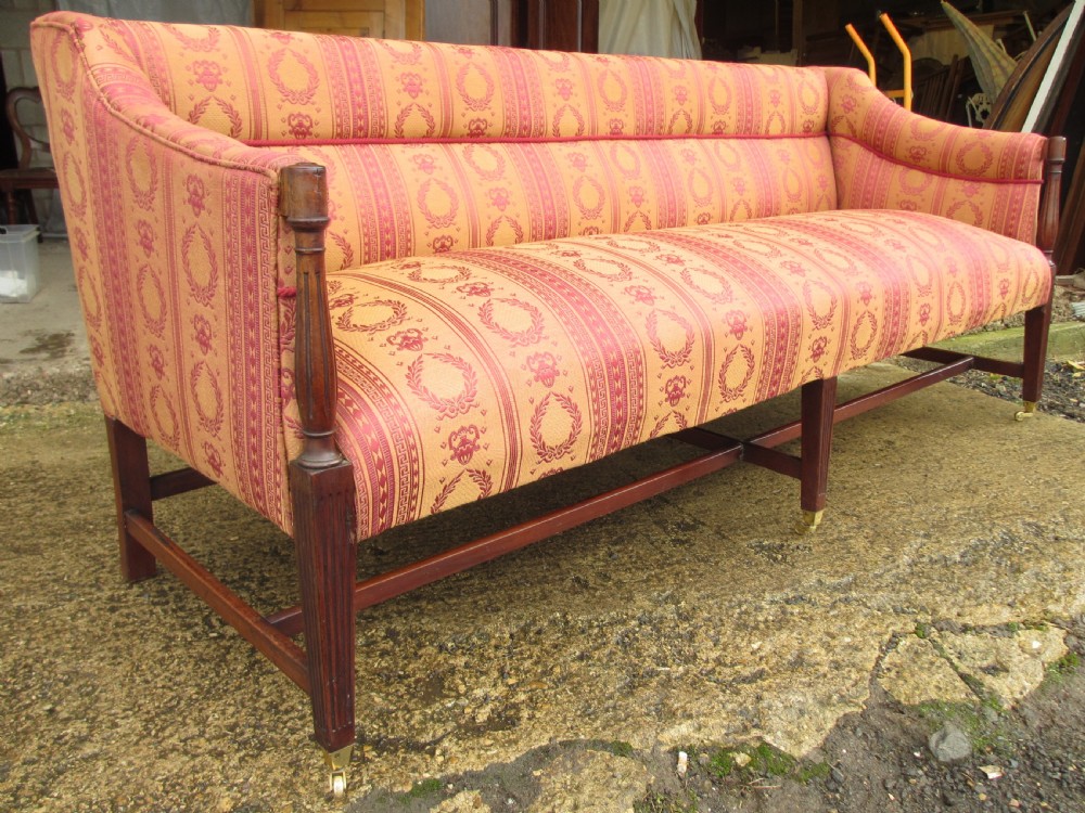 A Regency mahogany framed sofa upholstered in patterned red and gold fabric with reeded legs and brass castors. View II