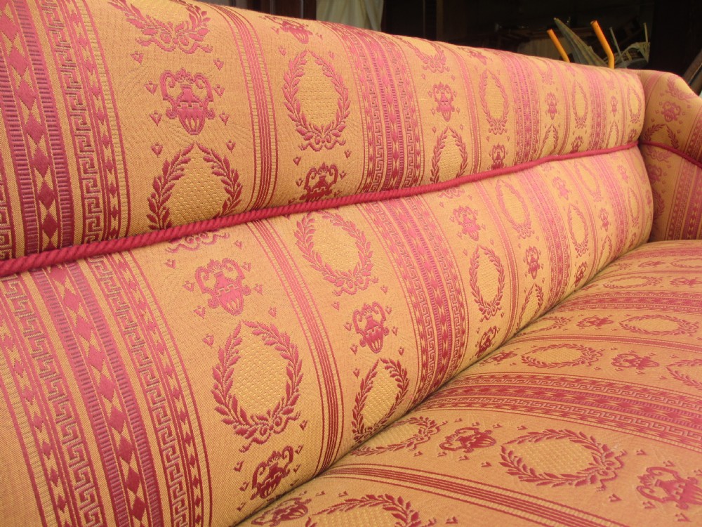 A Regency mahogany framed sofa upholstered in patterned red and gold fabric with reeded legs and brass castors. View III
