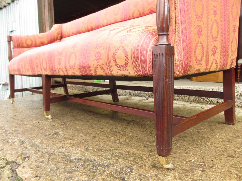 A Regency mahogany framed sofa upholstered in patterned red and gold fabric with reeded legs and brass castors. View VI